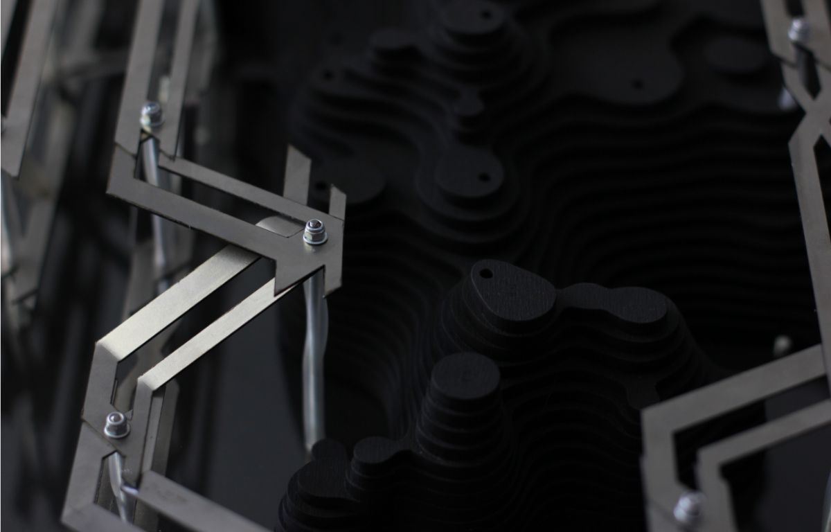 Close-up of fabricated model showing metal framework modules alongside dark layered wood components