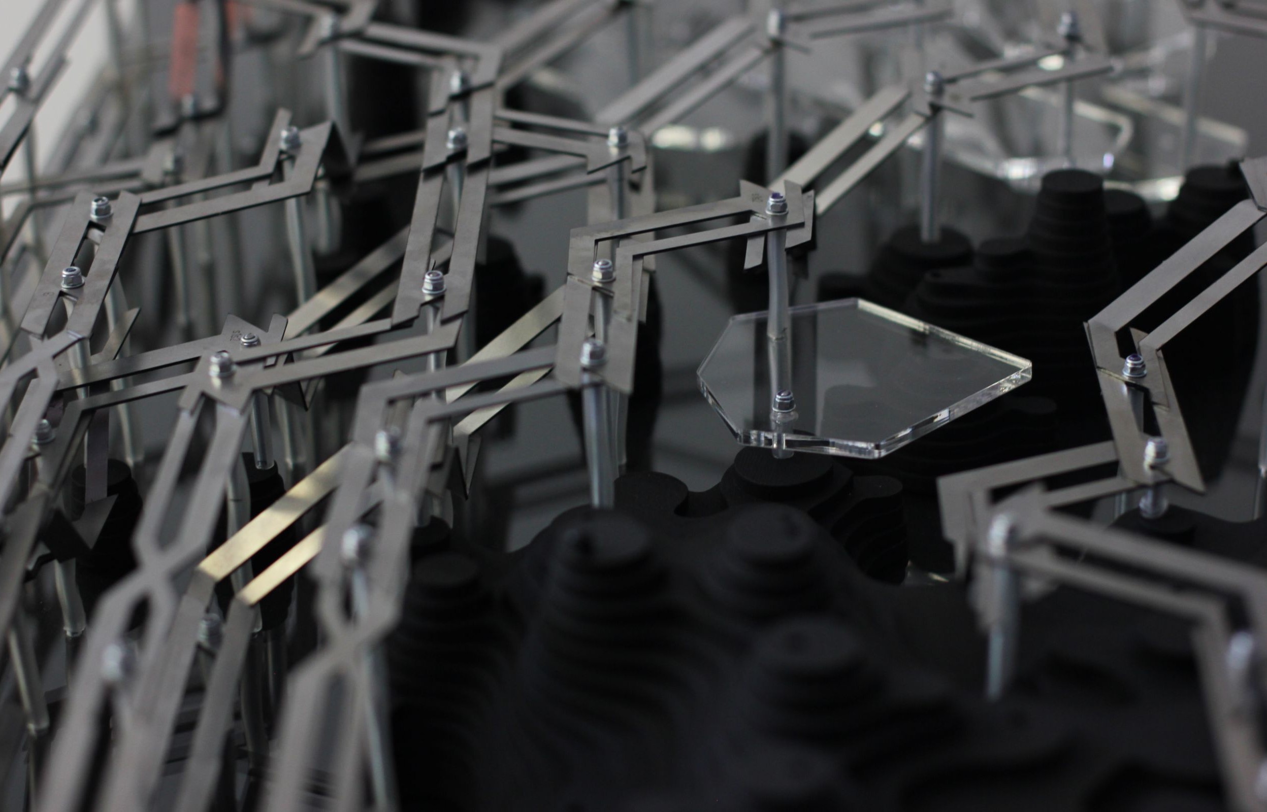 Close-up of fabricated model showing metal framework with acrylic panel alongside dark layered wood modules