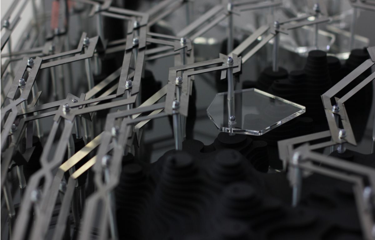 Close-up of fabricated model showing metal framework with acrylic panel alongside dark layered wood modules